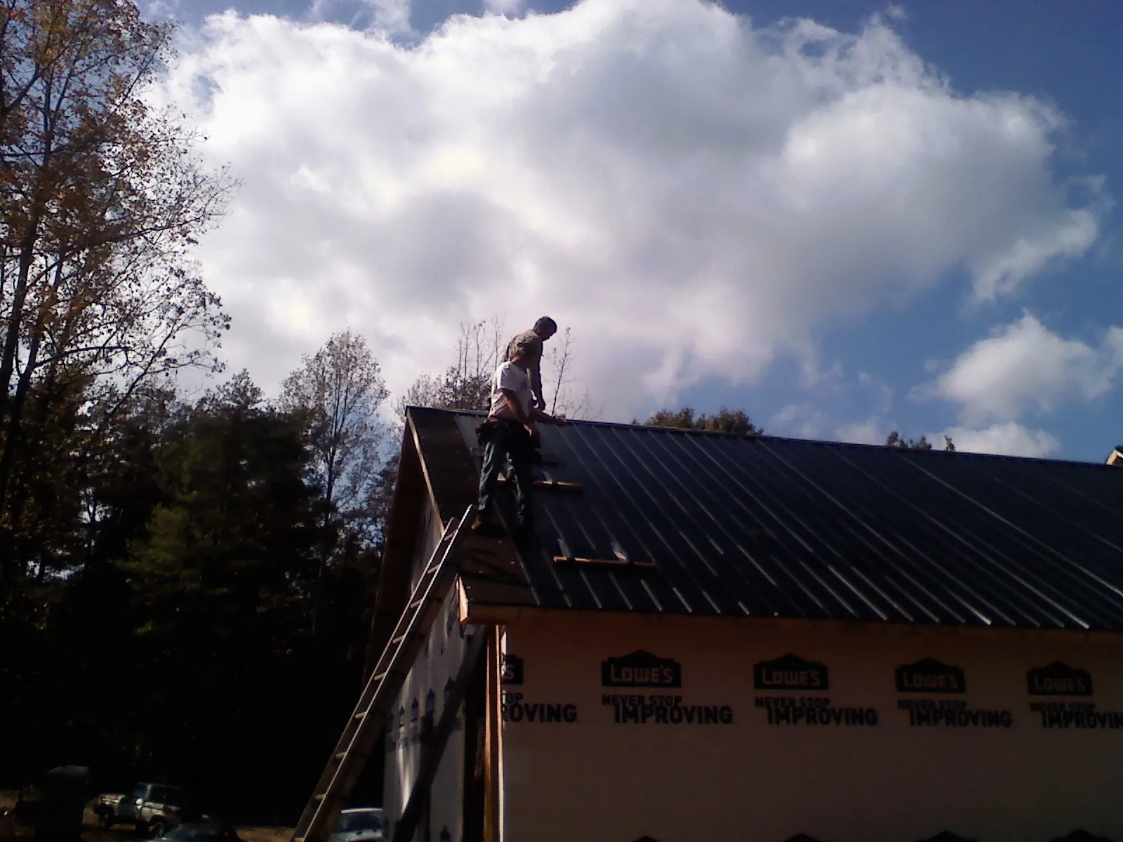 Roofer fastening dark metal panels high against a cloudy sky, from a Roof Inspection job in Palisades