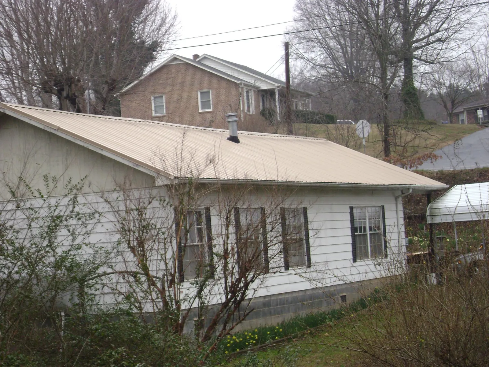 Tan metal roof on a white sided house set into a hillside — Commercial Roofing by Roofing Brothers in Palisades